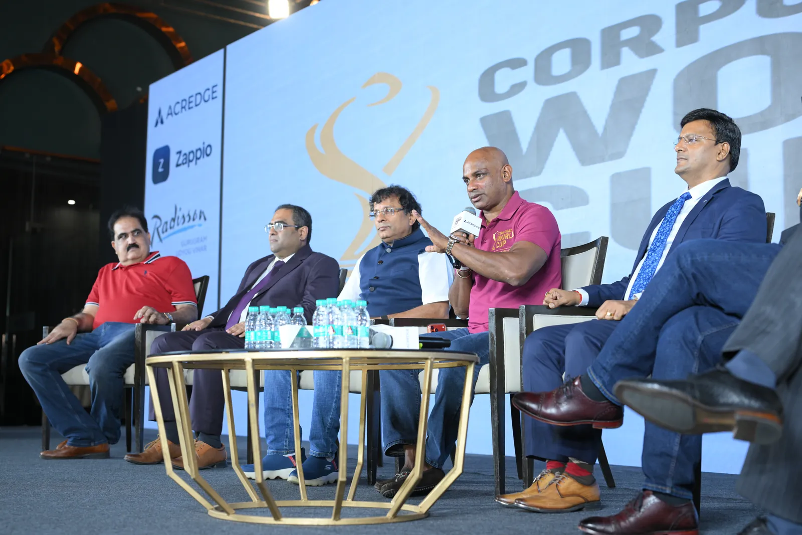 Panel discussion on stage at the Corporate World Cup launch event in Gurugram, with Acredge and Zappio on the backdrop